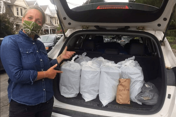 A delivery volunteer pointing to a trunk full of meal deliveries.