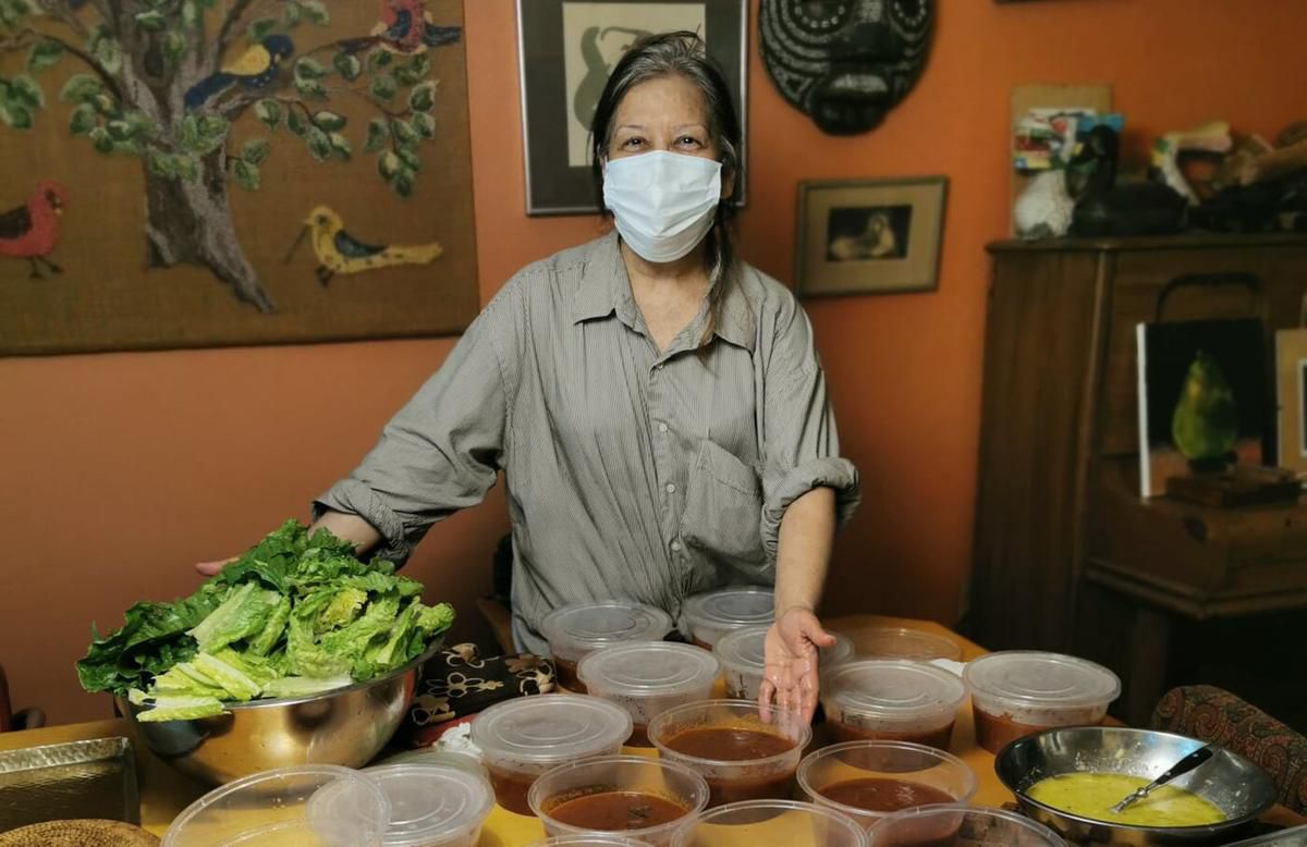 Woman wearing a mask and standing in front of an array of soups and salad.